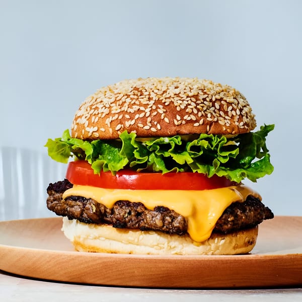 A Firebird Piri Piri Grill cheeseburger with lettuce and tomato on a wooden plate.