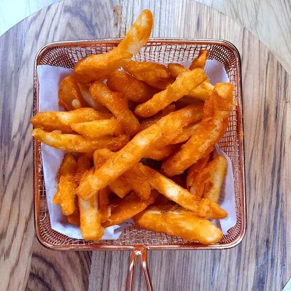 Golden-brown Piri Piri seasoned fries in a rose gold wire basket on a wooden table.